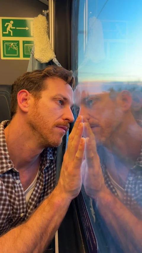 Man sitting by the window of a moving passenger train, gazing at the passing 库存影片 339197616