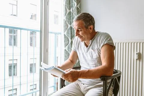 Man sitting at window reading folder with documents Stock Photos