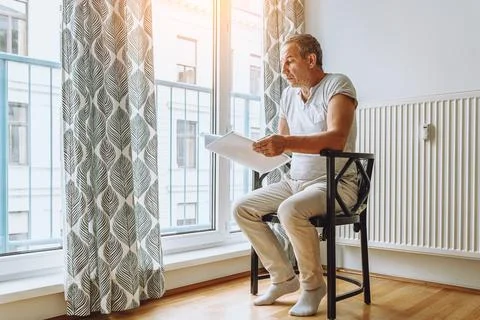 Man sitting at window reading folder with documents Stock Photos