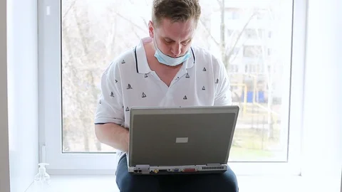 A man sitting on the windowsill of the house working on a computer Video stock 128002510