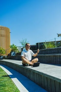 Man sitting on wooden platform using laptop and phone in outdoor space Stock Photos
