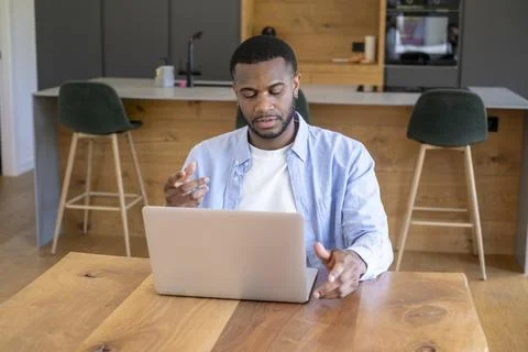 Man sitting at a wooden table using a laptop in a modern kitchen, engaging .. Stock Photos