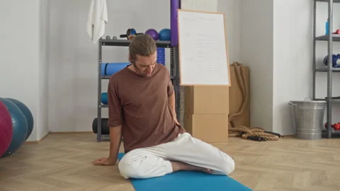Man sitting on yoga mat with hand on lower back showing backache in a studi.. Stock Footage 339192907