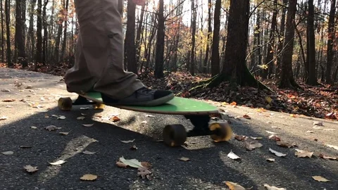 Man skating longboard on the leafs covered path towards the camera. Vídeo Stock 82515174
