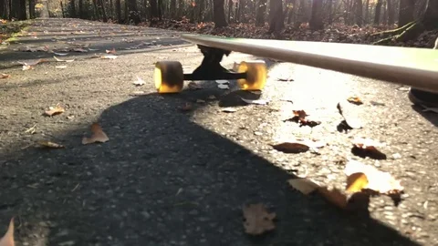 Man skating longboard towards the camera on the leafs covered path. Video stock 82516804