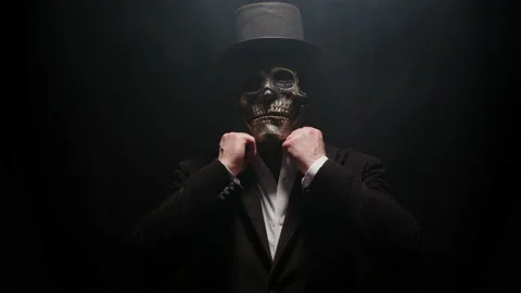 Man in skeleton suit in black jacket comes out of darkness and adjusts collar of Video stock 218325168