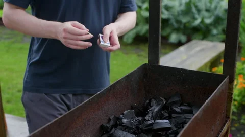 Man skillfully lighting charcoal in a barbecue grill for outdoor cooking Vidéo 296692074