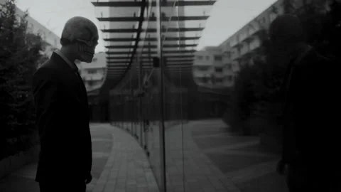 A man with a skull mask looking at his reflection in the building glass pane Stock-Footage 259889281