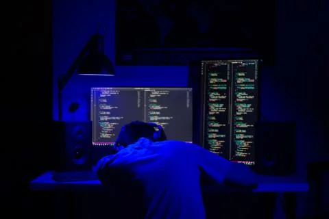 A man sleep at a computer in a room at a table at night with blue lighting an Stock-Fotos