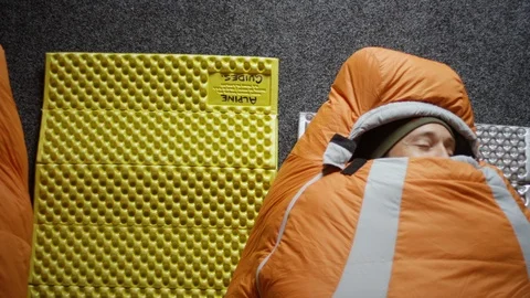 Man in sleeping bag rolls over to his friend in sleeping bag Stock Footage 116749204