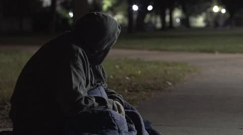 Man with sleeping bag sitting on sidewalk outdoors at night 4k Video stock 68985752