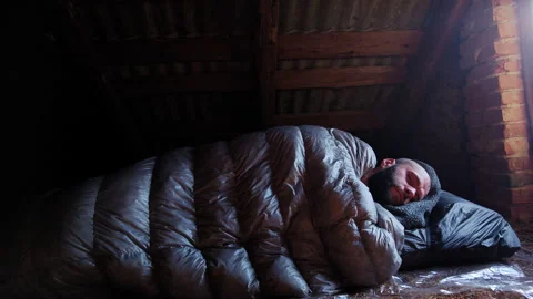 Man sleeping in black down sleeping bag under wooden attic roof Stock Footage 336971438