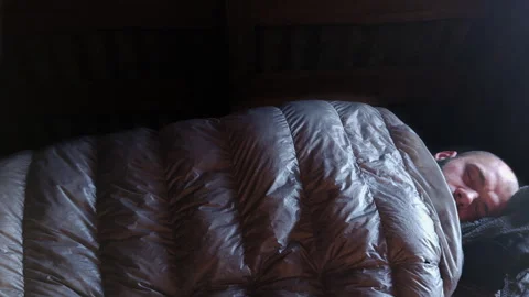 Man sleeping in black down sleeping bag under wooden attic roof Stock Footage 336971632
