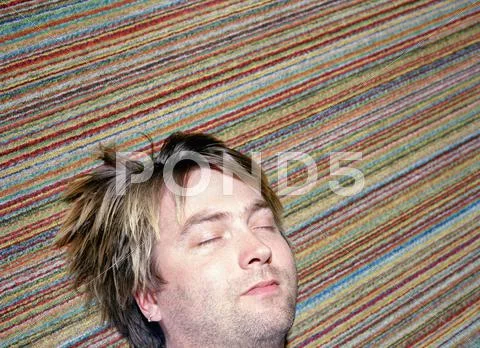 Man sleeping on multicolored carpet Stock Photos
