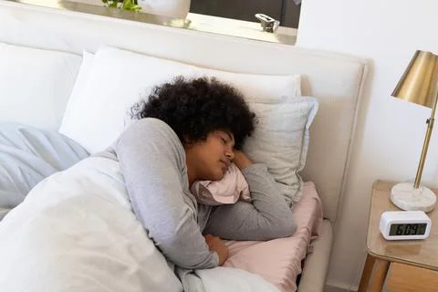 Man sleeping on right side on bed wearing light gray top with pillows, duvet, Stock Photos