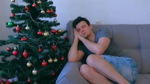Man sleeping sitting on couch at home near Christmas tree at eve waiting night. Stock Footage 136519429