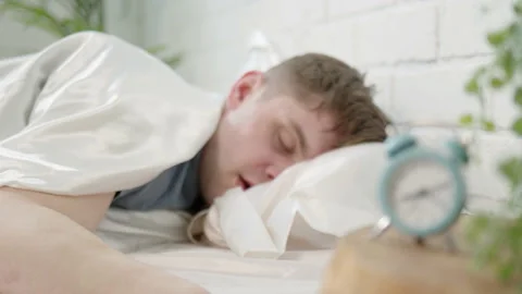 Man sleeps in bed with clock in foreground. concept of oversleeping for work or Stock Footage 172393146