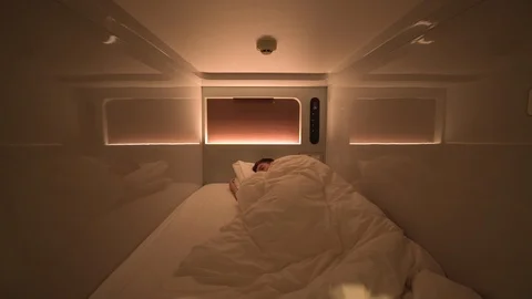 Man sleeps inside a clean modern capsule hotel room with lights and aircon Stock Footage 99069343