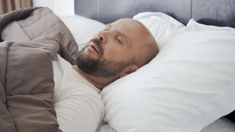 A man sleeps on a snow-white bed. Sweet morning dream. 스톡 동영상 119140321