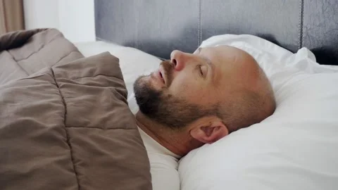 A man sleeps on a snow-white bed. Sweet morning dream. 動画素材 133417895