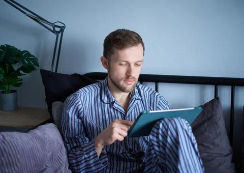 Man in sleepwear using tablet working, surfing or educating. Weekend concept 库存照片
