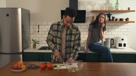 Man slices cucumber and playfully offers a bite to his smiling girlfriend. Stock Footage 305654292