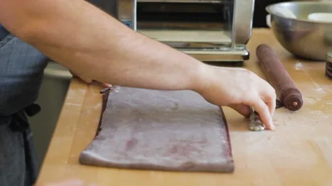 Man slices pasta dough with a roller blade and patting the beet purple pasta Stock Footage 199153066