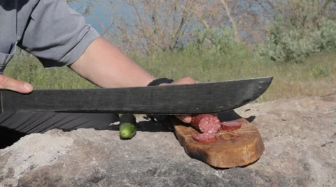 Man slices salami on the stone using a machete Stock Footage 62476973