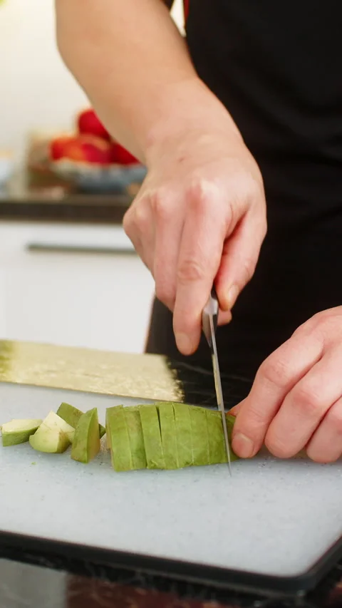 Man slicing avocado on cutting board in home kitchen preparing healthy balanced Stock Footage 347055489