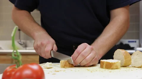 A man slicing bread with a knife in a kitchen on a cutting board. Stock Footage 57400478