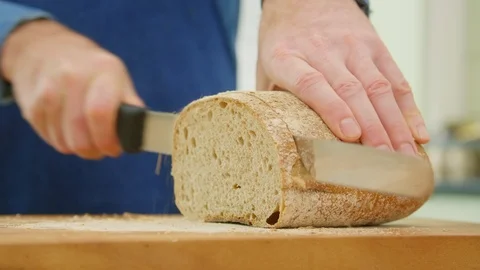Man Slicing Crusty Loaf Of Bread With Knife In Kitchen Stock Footage 86115113