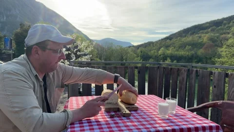 Man slicing fresh bread on rustic terrace outdoors 스톡 동영상 333526057