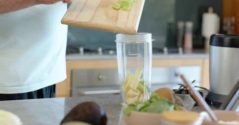 Man is slicing fruit on board at counter, holding angled board over blender cup Stock Footage 339559068