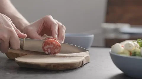 Man slicing salame on olive wood board on concrete countertop Stock Photos