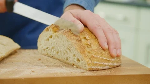 Man Slicing Sourdough Bread With Knife On Cutting Board In Kitchen Stock Footage 86072367