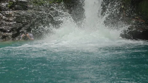 Man Slides Down Natural Waterfall Into Turquoise Pool in Tropical Rainforest. Stock Footage 338370667
