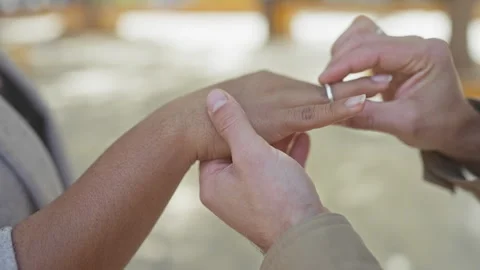 A man slides an engagement ring onto a woman's finger outdoors, symbolizing.. Stock Footage 282579988