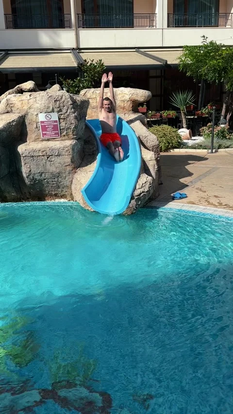 Man sliding down blue water slide into backyard pool Stock Footage 345495849