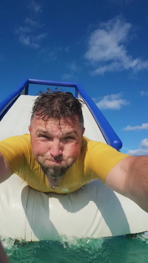 Man Sliding Down Inflatable Water Slide Into Ocean on Sunny Summer Day. Stock Footage 338369209