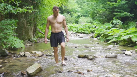 A man in slippers walking on a stream in the forest. Vídeo Stock 212436294