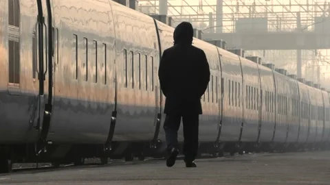 A man slow walks alone on a platform in front of a slow moving train Stock Footage 169253019