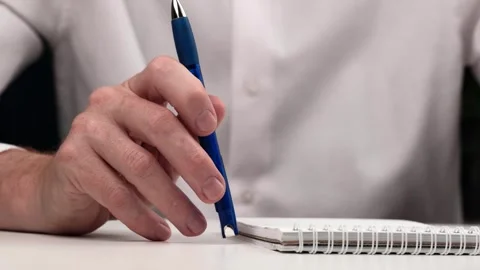 Man slowly and thoughtfully taps a blue pen on table next to notebook. closeup. Stock Footage 255942440