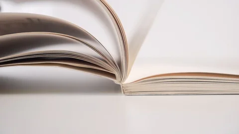 A man slowly flips through the pages of a paperback book on a white backgroun Stock Footage 121800882