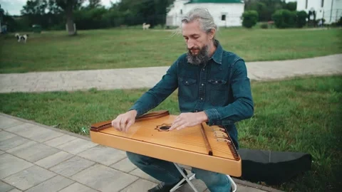 A man slowly plays the harp while sitting on the street. Stock Footage 152657780