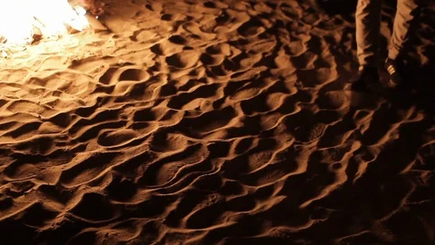 Man slowly strolls around the reflections from the fire flame play on the sand Stock Footage 115930104