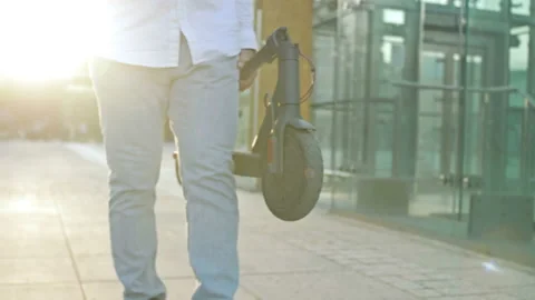 Man slowly walks down a city street and carries a folded electric scooter. Stock Footage 201728198