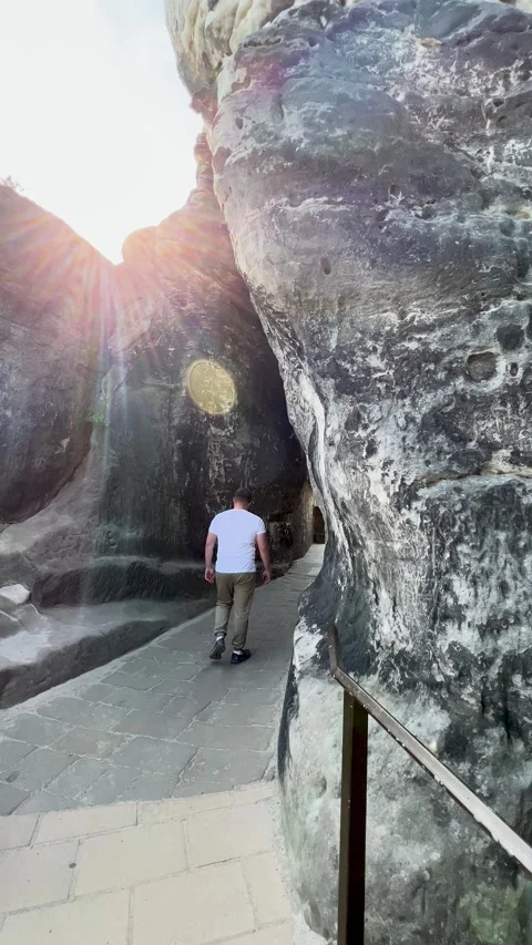 A man slowly walks towards a bright light in a picturesque rock formation Stock Footage 303894489