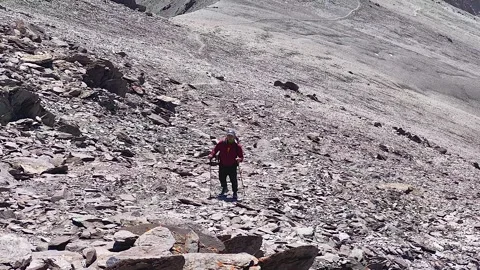 Man with a small backpack and trekking poles walks along a rocky trail Video stock 249149362