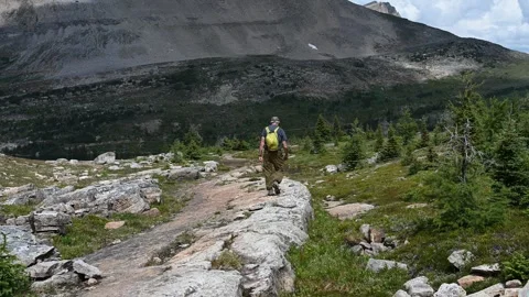 Man with a small lime green packsack is walking along a rocky ledge  Stock Footage 261467046