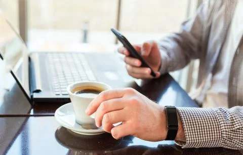 Man in smart watch drinking coffee on work space. Man using laptop, holding s Stock Photos